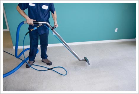 person in blue work cloths using a cleaning device on the floor